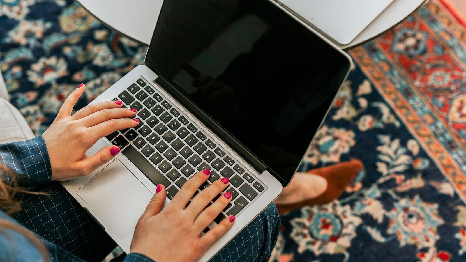 From above, the gaze falls on a woman holding a laptop on her lap and typing 