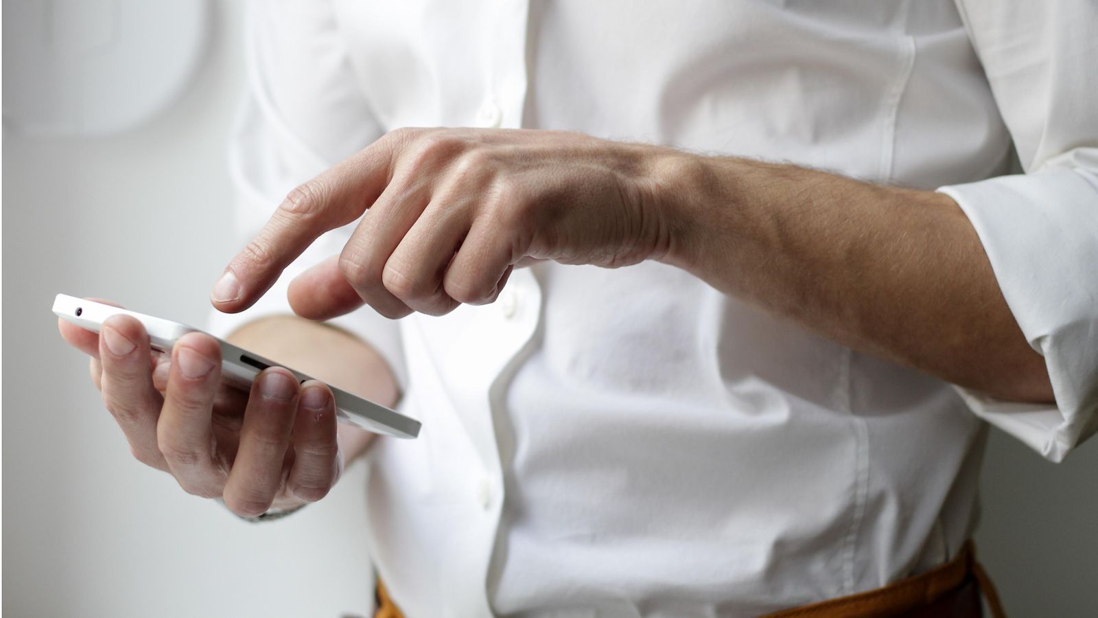 A man in a white shirt is typing on his smartphone