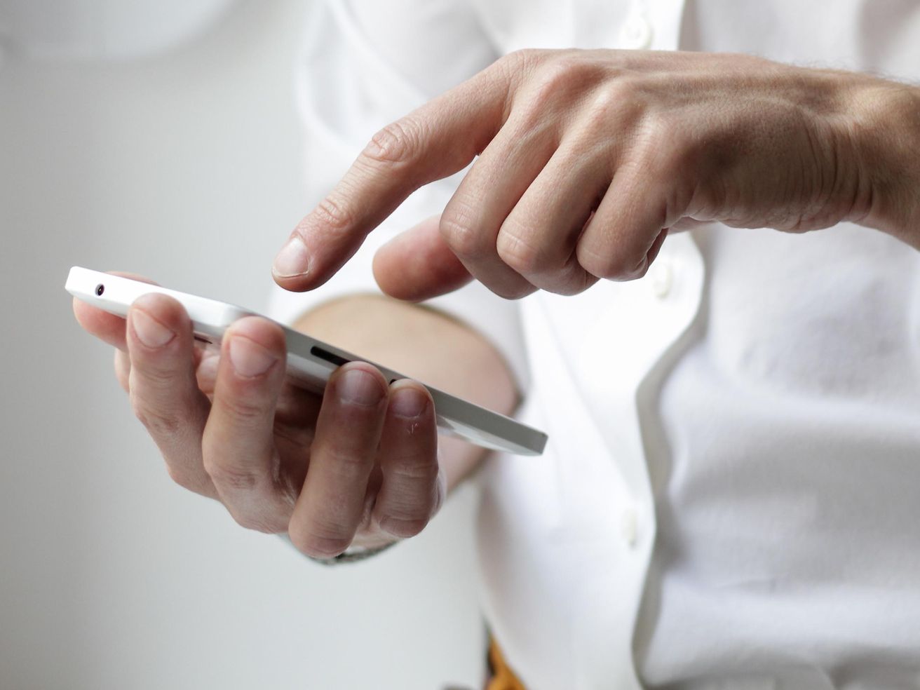 A man in a white shirt is typing on his smartphone