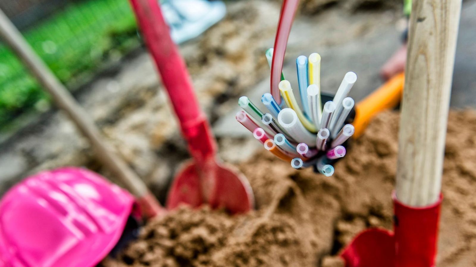 Fiber optic cables protrude from the ground, shovels and a helmet can be seen next to them